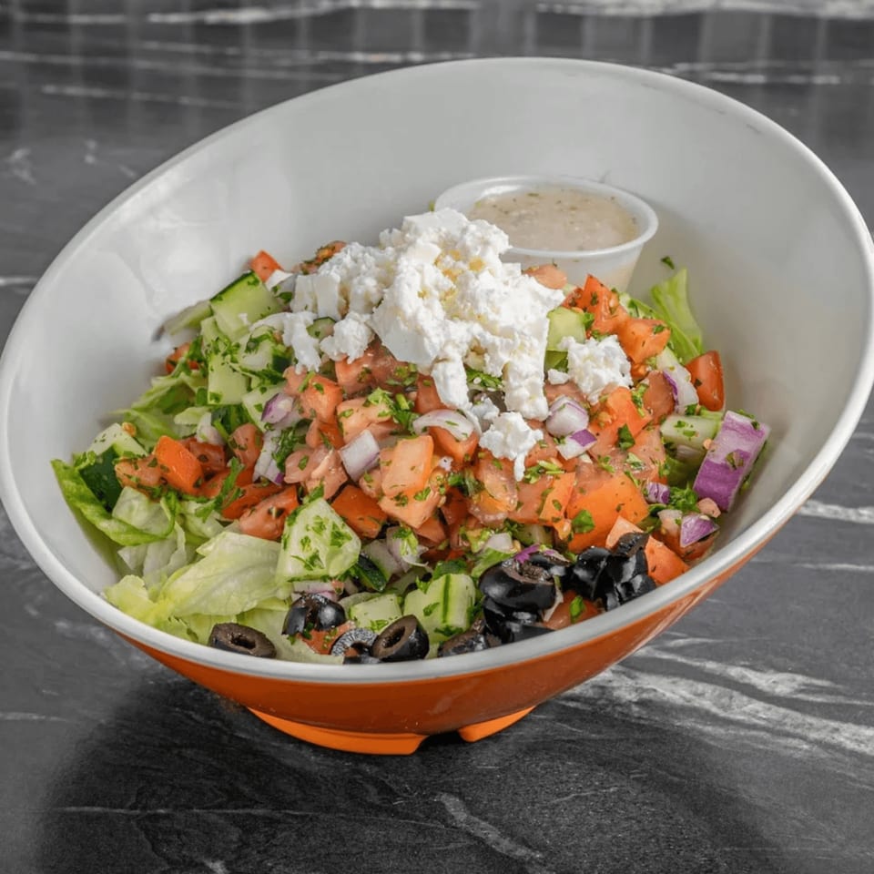 A vibrant Greek salad with lettuce, tomatoes, cucumbers, olives, red onions, and feta cheese.