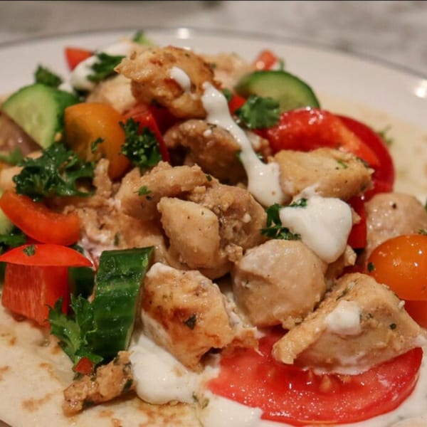 Chicken gyros with tomatoes, cucumbers, and creamy white sauce on a flatbread.