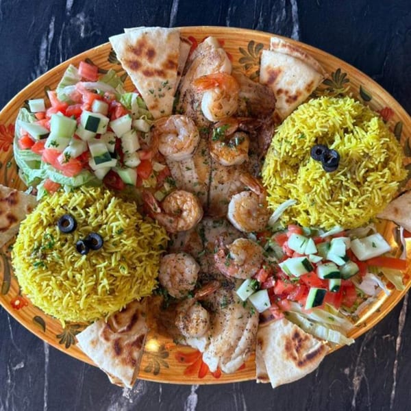 A Greek platter with grilled shrimp, fish, yellow rice, pita bread, and two fresh salads.