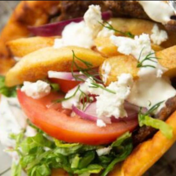 Close-up of a Juicy Gyros pita with meat, fries, tomato, onion, lettuce, feta, and dill.